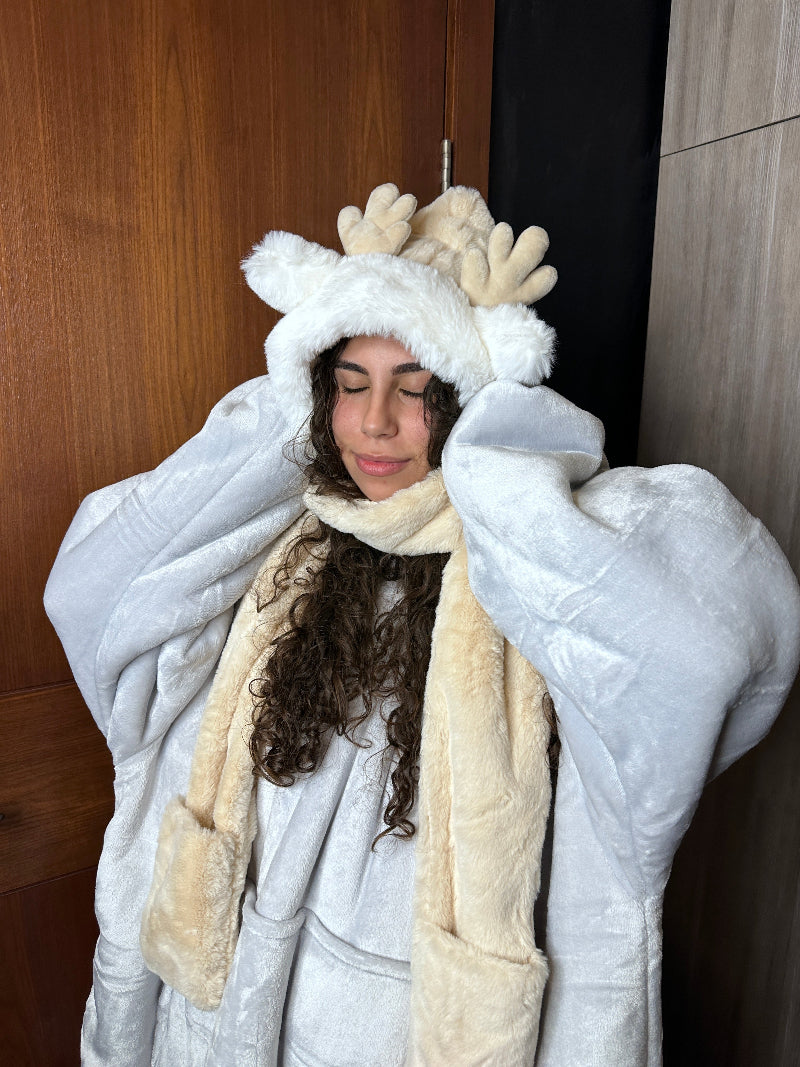A close-up of a woman wearing a beige Cozify plush hoodie with white trim and soft furry texture, featuring cute reindeer antlers on the hood and her face partly visible.