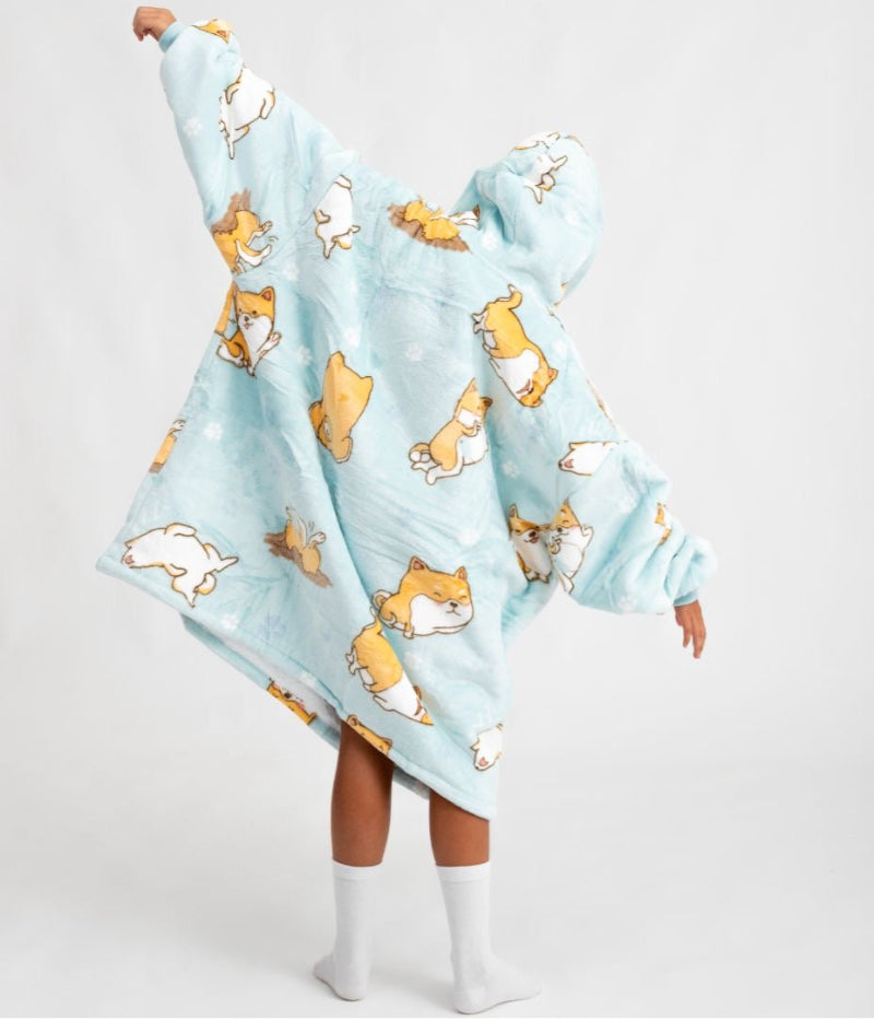 Back view of a child wearing a light blue Cozify wearable blanket hoodie with an all-over print of playful corgi dogs in various poses. The hoodie has a soft, cozy texture and an oversized fit.