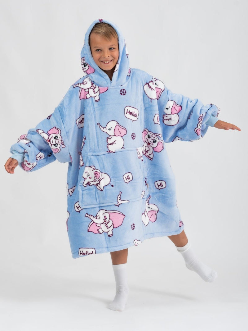 A smiling child wearing a light blue oversized hoodie with a pink elephant cartoon print. The hoodie features speech bubbles with "Hello!" and "Hi", and has a large front pocket and hood. The child poses playfully with one foot up and arms spread wide, wearing white socks.