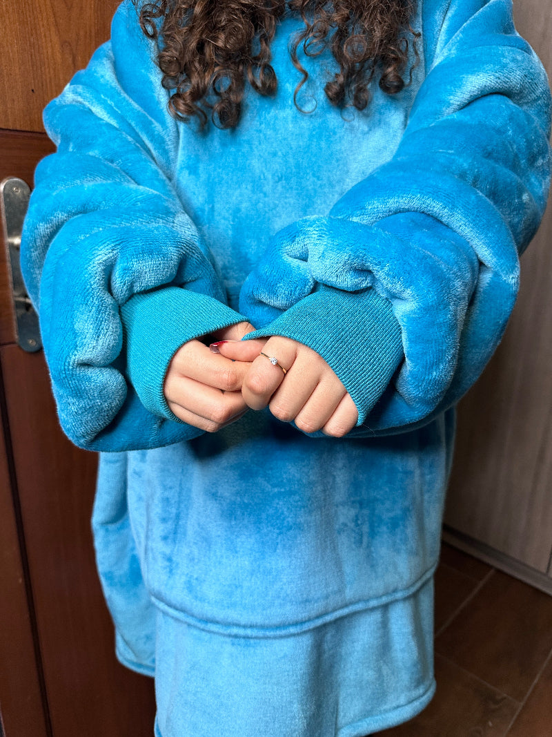 A close-up view of a person wearing a blue Cozify oversized wearable blanket hoodie, showing the plush texture and long sleeves with ribbed cuffs.