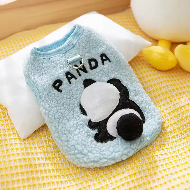 Flat lay of a light blue sherpa fleece pet vest by Cozify, featuring a black and white panda design and the word "PANDA" embroidered on the back, with a metal D-ring at the neck for leash attachment, displayed on a yellow textured blanket.