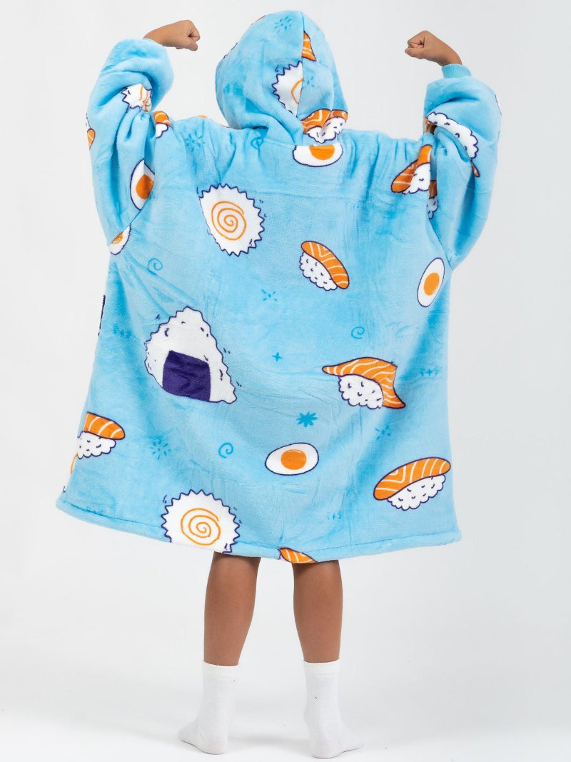 Back view of a child wearing a bright blue Cozify wearable blanket hoodie featuring a playful sushi-themed print with cartoon rice balls, eggs, and rolls. The oversized hoodie has a cozy, sherpa-lined texture and the child is posing with both arms flexed upward.
