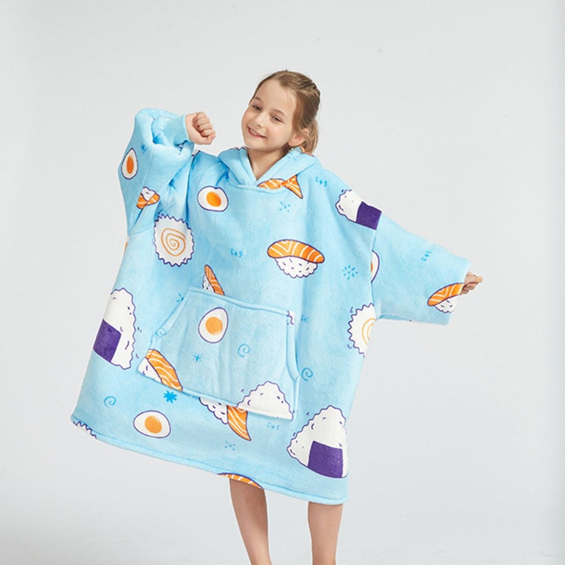 Front view of a child wearing a light blue Cozify wearable blanket hoodie with a fun sushi print, featuring cartoon rice balls, eggs, and sushi rolls. The hoodie is oversized and sherpa-lined for warmth, and the child poses playfully with arms slightly bent and a smile.