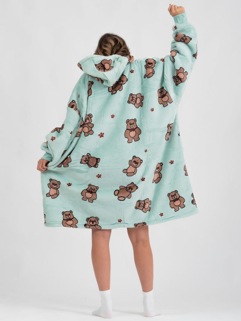 Back view of a person wearing a light blue oversized hoodie with an all-over teddy bear and paw print design, featuring a hood and relaxed fit, one arm raised playfully.