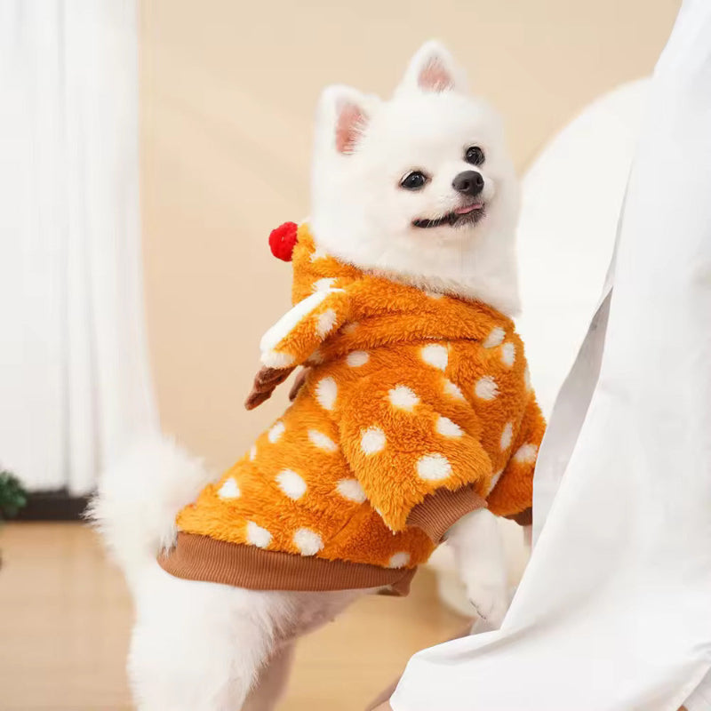 White fluffy dog standing with front paws on a chair, wearing a cozy brown reindeer hoodie with white polka dots, antlers, and a red pom-pom nose. Side view of festive pet outfit by Cozify.