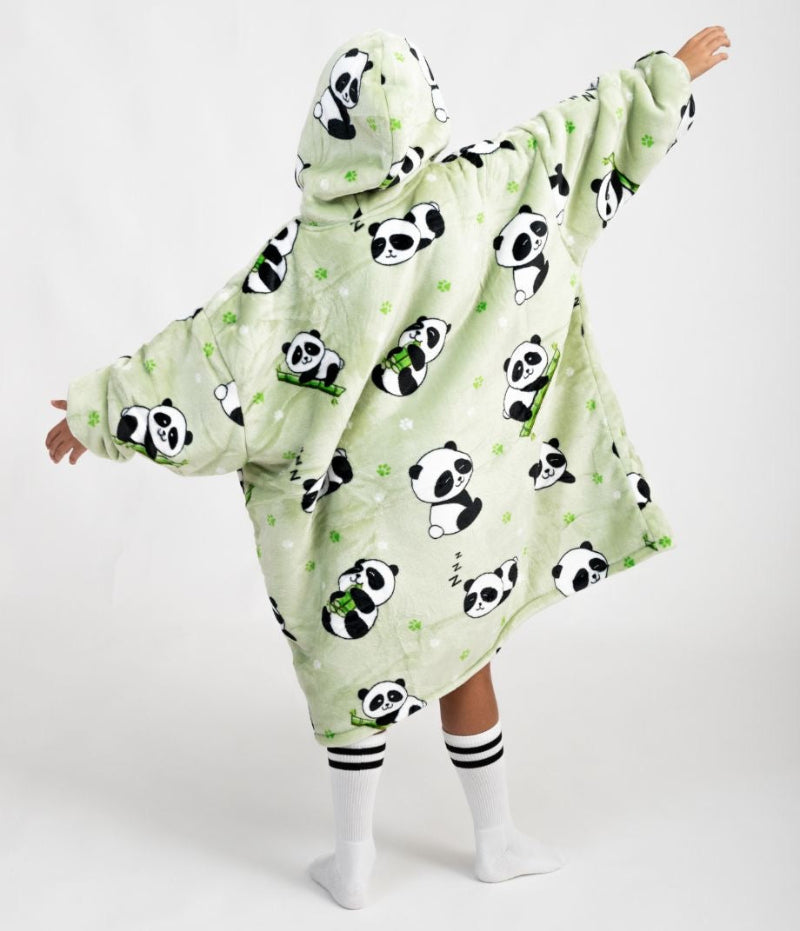 Back view of a person in a light green oversized hoodie featuring cute panda and bamboo illustrations, arms outstretched, hood up, wearing knee-high white socks with black stripes.