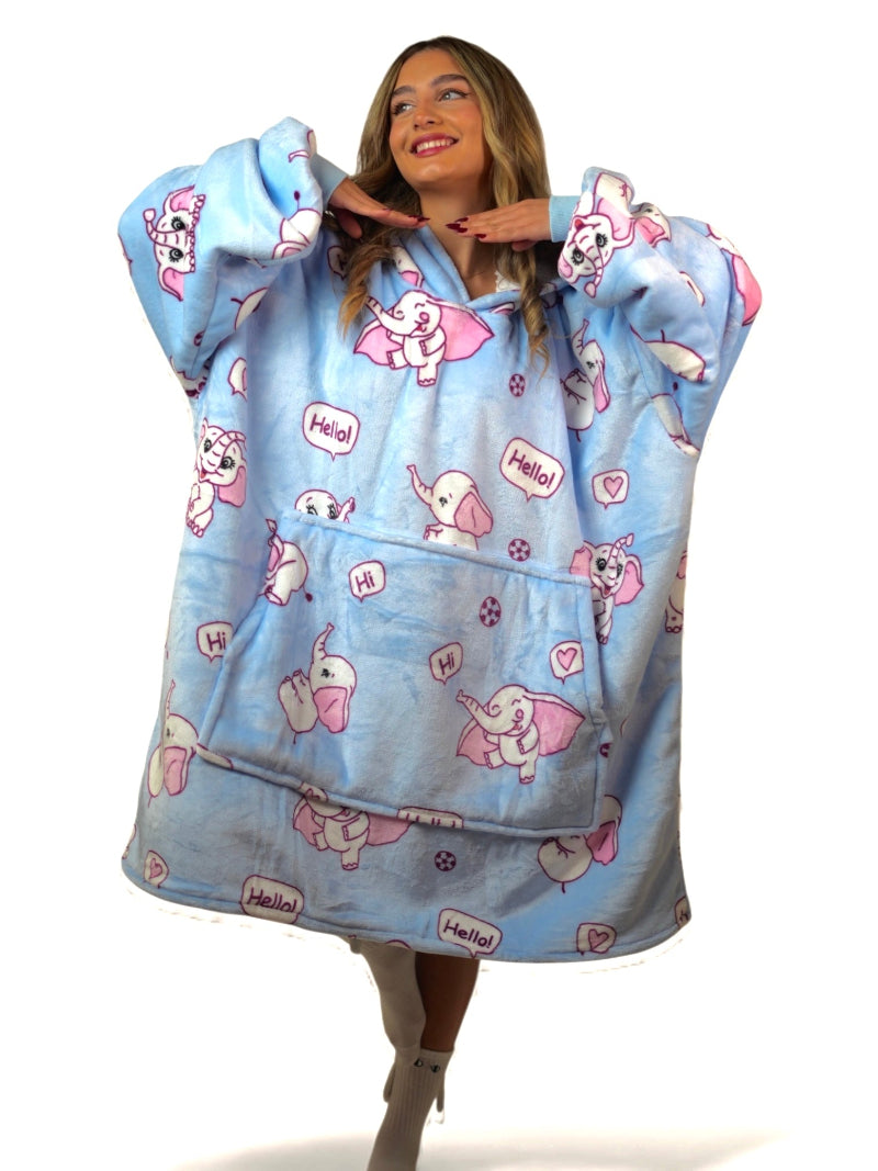 Smiling woman in a light blue oversized Cozify hoodie blanket featuring a playful pink elephant print with speech bubbles and hearts.