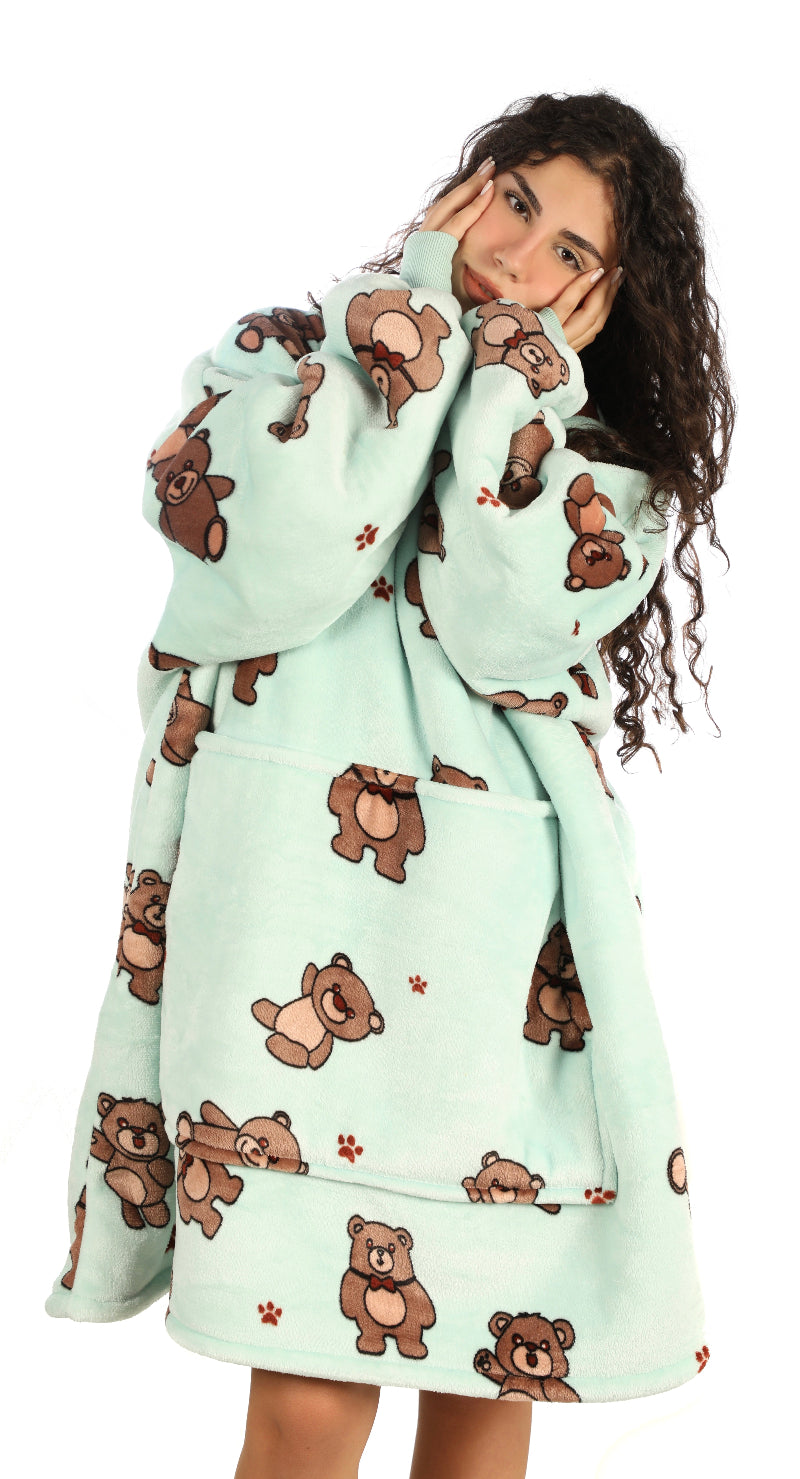 A woman wearing a mint green Cozify oversized wearable blanket hoodie with an adorable brown bear and paw print pattern, shown from the front in a cozy, relaxed pose.