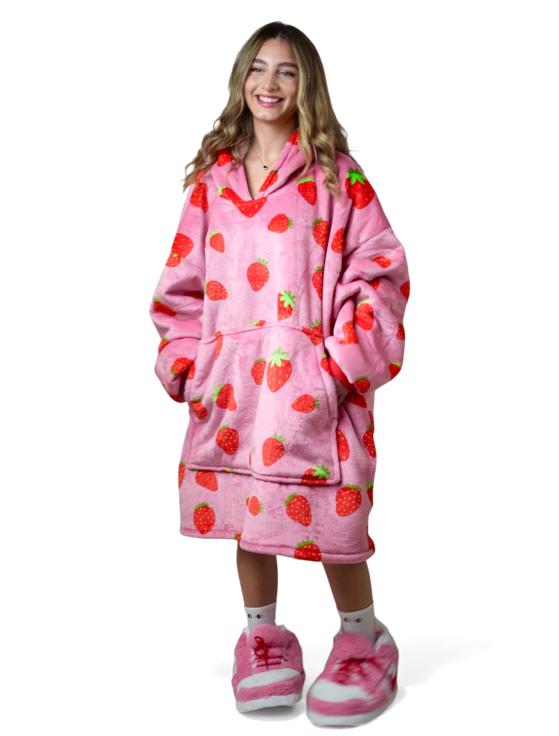 Smiling woman wearing a matching Cozify bundle with a pink oversized strawberry-print sherpa hoodie blanket and coordinating pink fuzzy slippers.