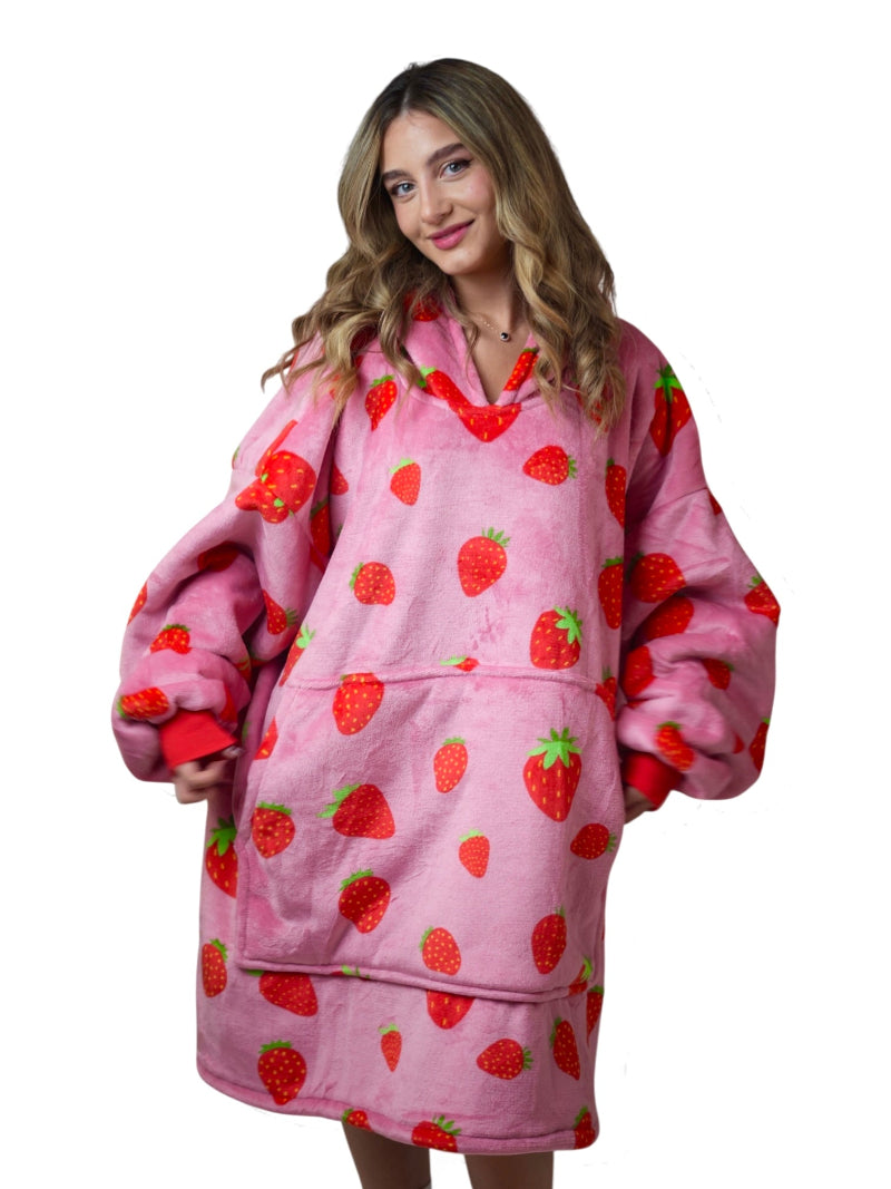 Woman smiling in a pink oversized Cozify sherpa-lined hoodie blanket featuring a playful red strawberry print and a large front pocket.