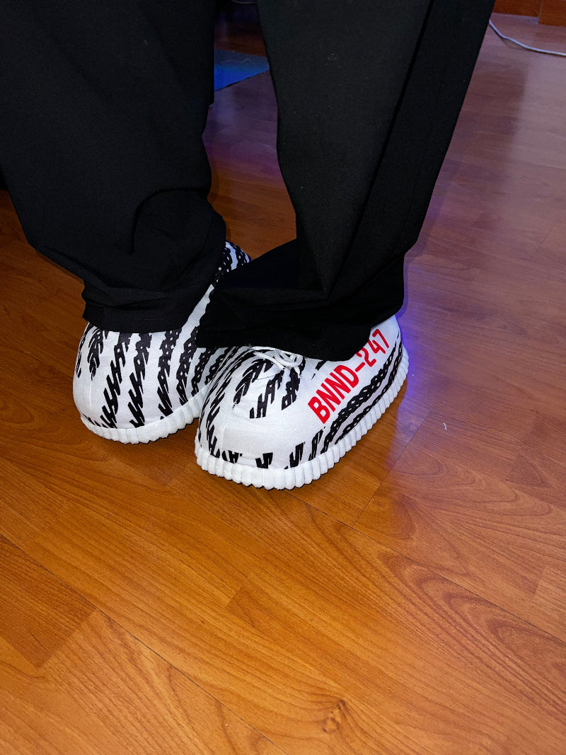 Close-up of Cozify black and white striped fuzzy slippers with red lettering, worn indoors on a wooden floor.