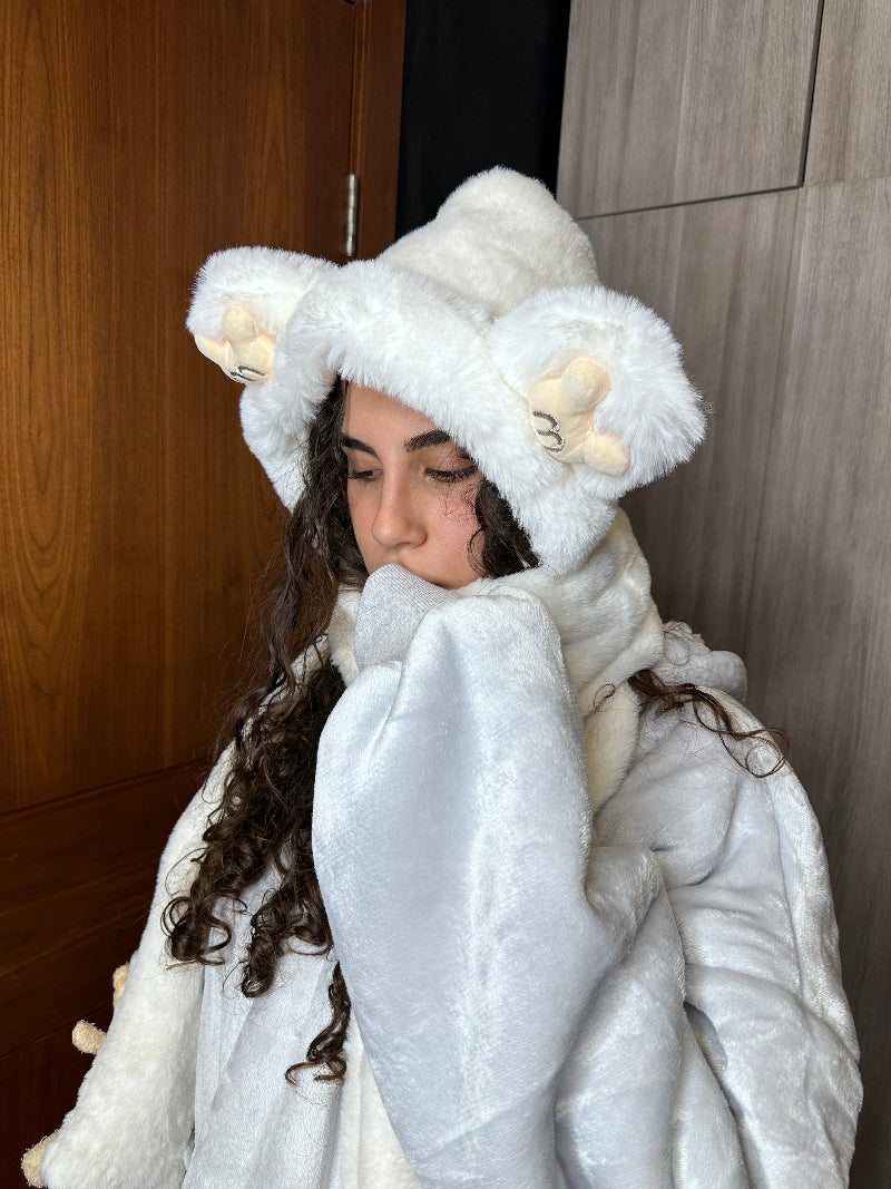 A woman wearing a white Cozify plush wearable blanket hoodie with a cozy soft texture, featuring an attached teddy bear detail hanging from the front pocket.