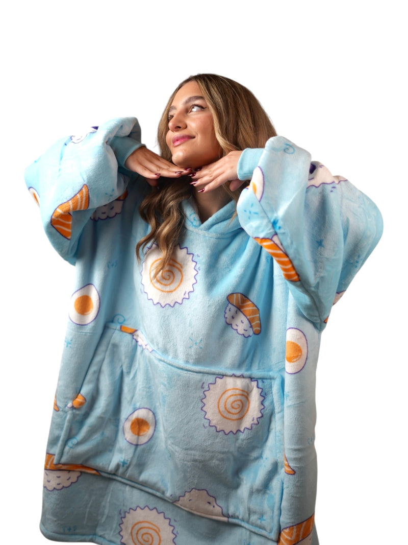 Smiling woman posing in a light blue oversized wearable blanket hoodie with a sushi print and a front pocket, shown close-up against a white background.